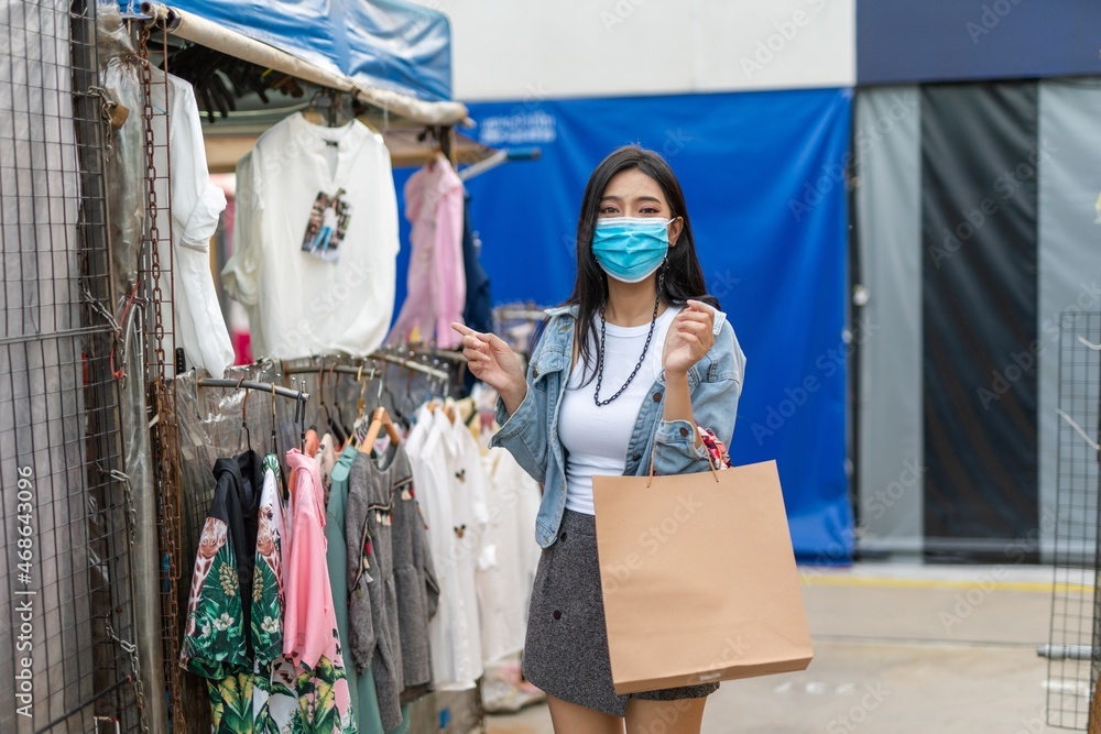 Beautiful asian female young model lady wearing mask having a solo shopping by herself and looking through concentratedly some fashion product put on sale at a fashion store in a night market 