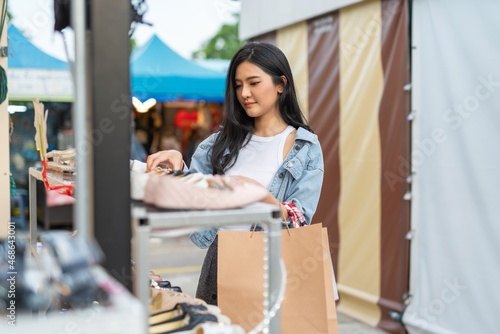 Beautiful asian female young model lady having a solo shopping and stroll walk time by herself and looking through concentratedly some fashion dresses put on sale at a fashion store in a night market 