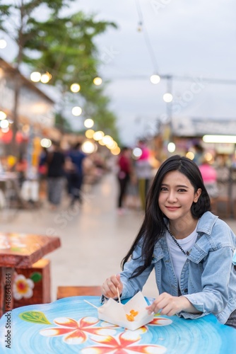 Beautiful asian female young model lady having a stroll walk relaxingly and eating delicious and tasty street food from the food bazaar in a night market happily and cheerfully