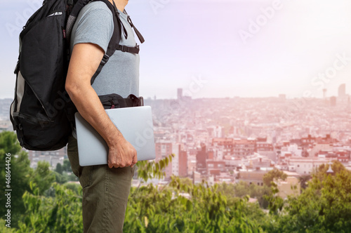 Unrecognizable digital nomad man traveling the world working with his laptop with a background city photo