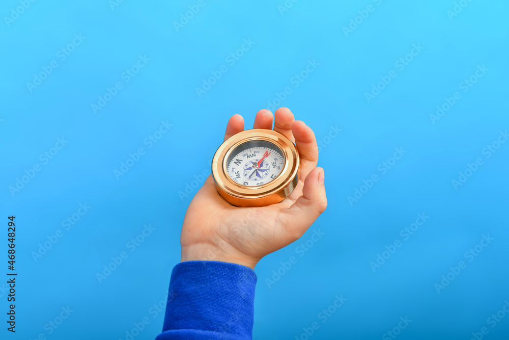 The boy holds a compass in his hand on a blue background.