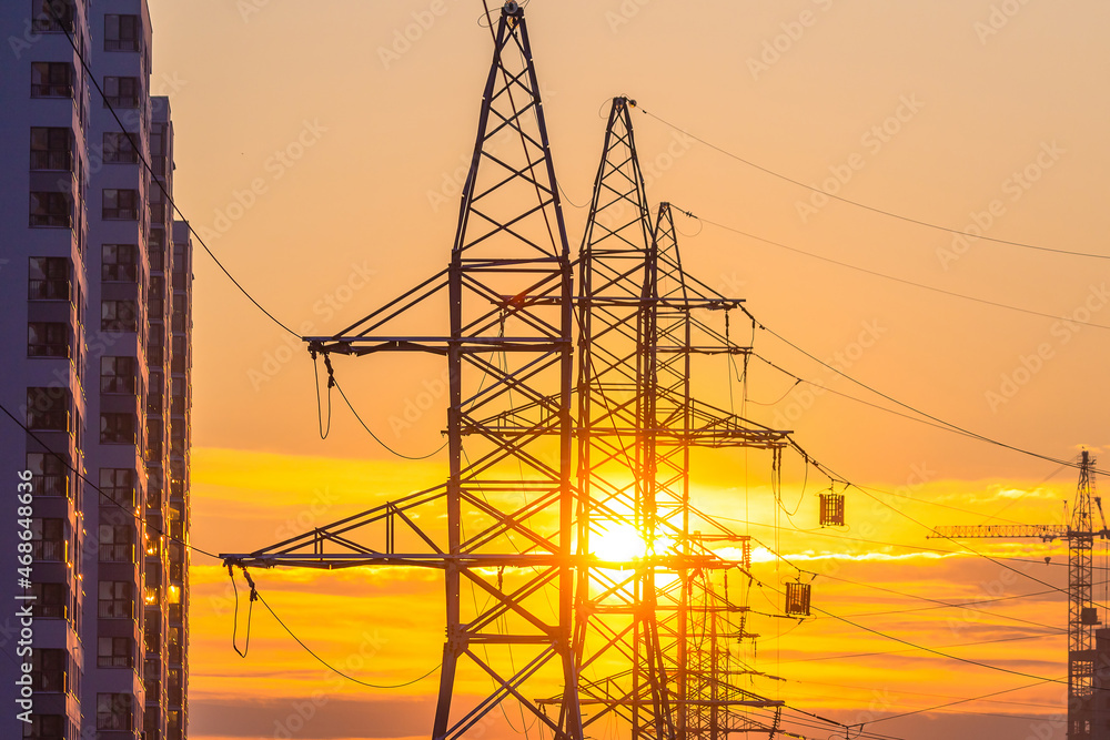 high-voltage pole with wires on the background of sunset and houses