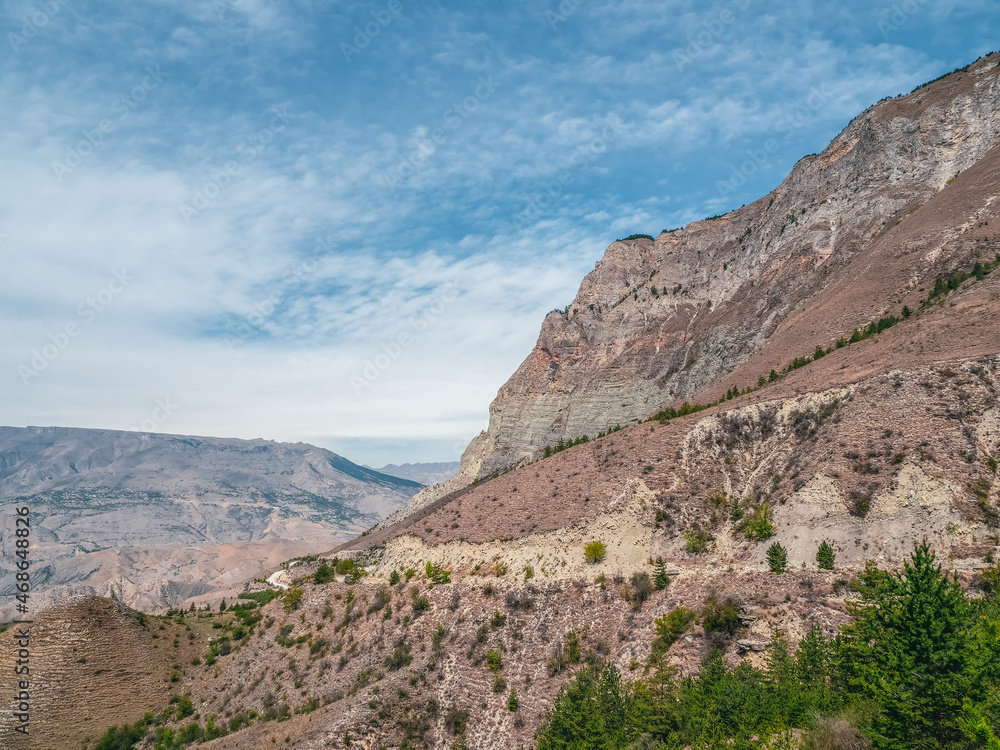 Mountain texture, mountain terrain. Colorful sunny morning landscape with silhouettes of big rocky mountains. Dangerous narrow dirt mountain road through the hills