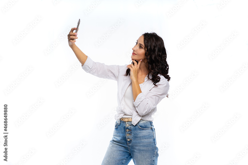 portrait of a woman with a phone in the studio on a white background. White shirt, blue jeans, black hair. beautiful model