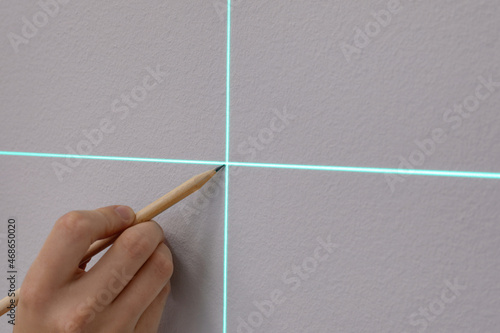 Fotografie Woman using cross line laser level and pencil for accurate measurement on grey w