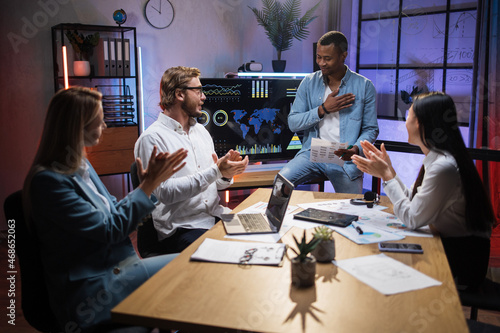 Multi ethnic company workers applauding to his african colleague during working meeting at modern office. Four people gathering at room for planning business strategy.