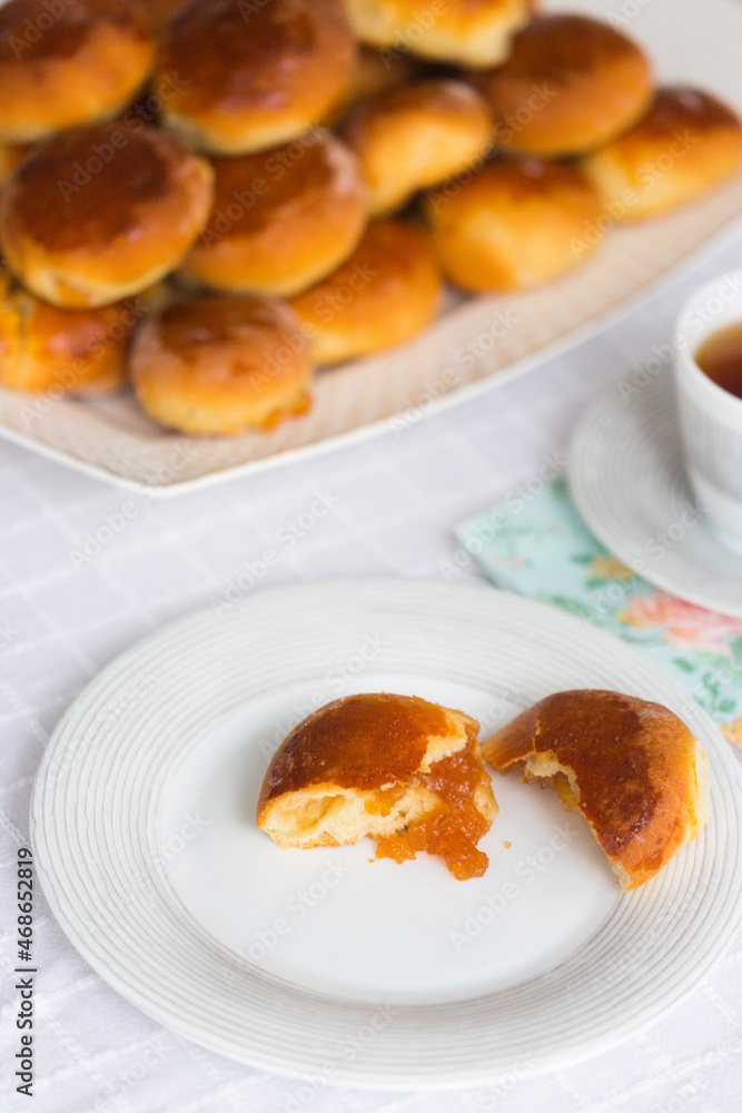 Russian traditional pies or pirozhki with apple jam on white platter on white tablecloth Russian traditional pies or pirozhki with apple jam on white platter on white tablecloth