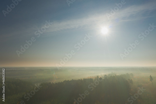 Poranne mgły oświetlone słonecznymi promieniami unoszące się nad lasem. Widok z drona. © boguslavus