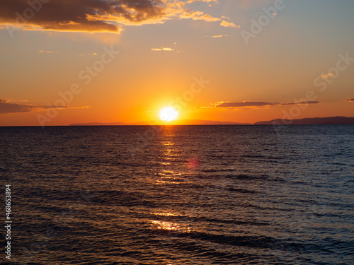 Beautiful seaside sunset - sun going down behind distant mountains