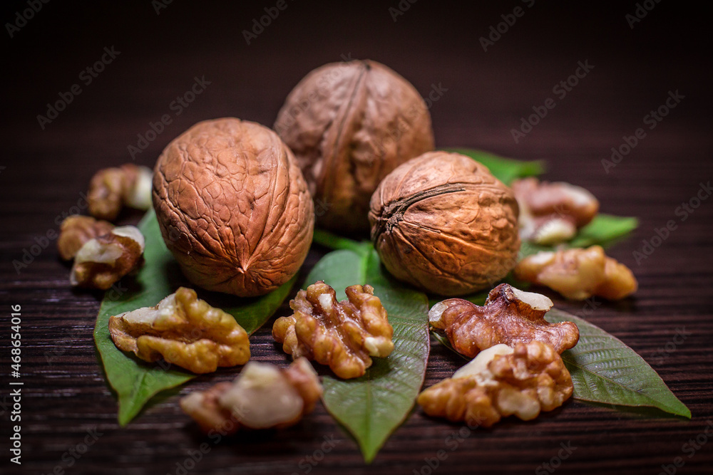 Fototapeta premium Walnuts - shelled and kernels with green walnut tree leaves isolated on dark background