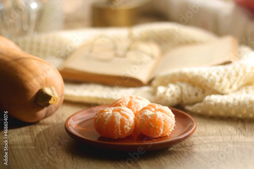 Peeled tangerines, butternut squash, open book, reading glasses and cozy blanklet. Hygge at home. Selective focus. photo