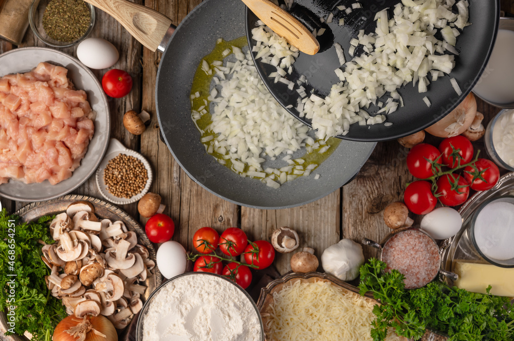 The cook fries onions in a skillet. Ingredients for making salad, pizza, pie, ravioli. Large group of objects. Wooden texture. High angle view. Restaurant, hotel, cafe, pizzeria.