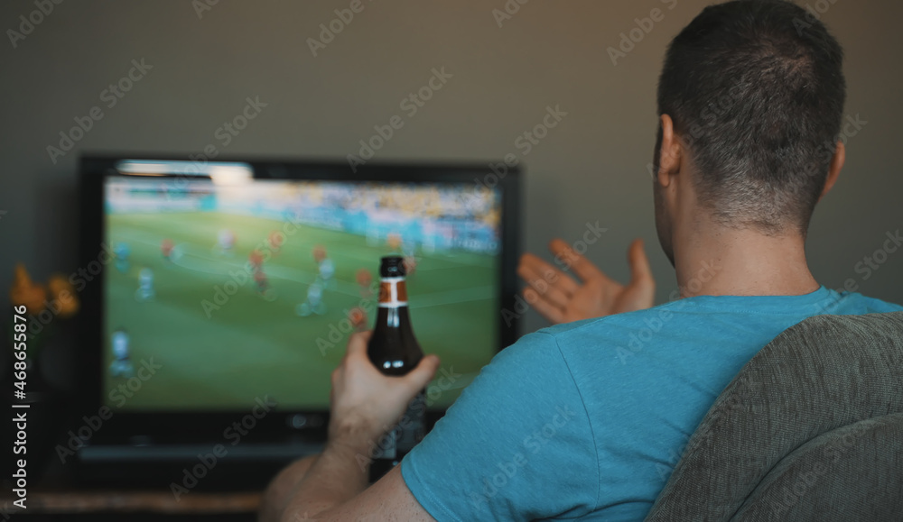 Naklejka premium Man with bottle of beer watching football on TV.