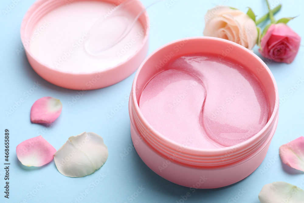 Under eye patches in jar and rose flowers on light blue background, closeup. Cosmetic product Under eye patches in jar and rose flowers on light blue background, closeup. Cosmetic product
