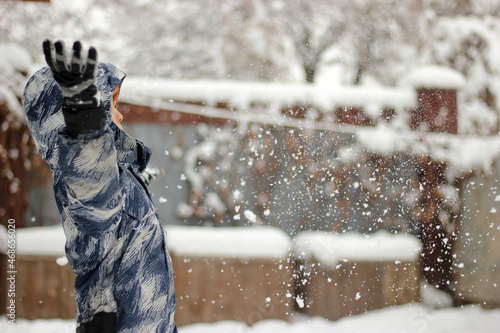 Boy in overalls and gloves rejoices in the falling snow
