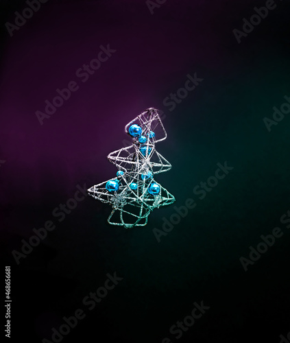 Silver Christmas tree with metallic blue baubles in vivid neon colours. Dark background. Cyberpunk aesthetic concept.