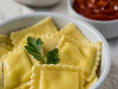 Close-up. Portion of Italian ravioli drizzled with melted butter and a parsley leaf. In the background there are two sauces and sour cream. Restaurant, hotel, culinary blog, menu design.
