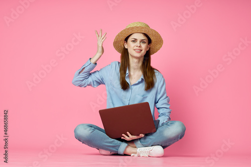 cheerful woman with laptop sitting on the floor on a pink background