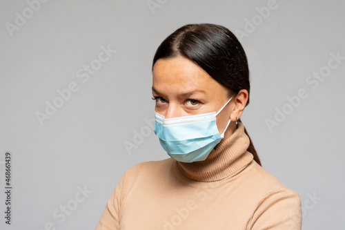 A calm and confident young woman in a medical mask on a gray background, protected by vaccination against a pandemic.