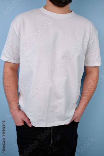 Man in a white T-shirt poses near a blue wall. Hand gestures and emotions. Studio photography. The concept of emotion, strength and fun. Casual wear. Space for inscriptions and logo