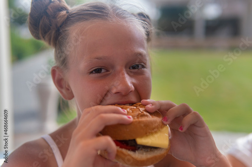 teen girl eating hamburgerand laughing on the balcony on a sunny day