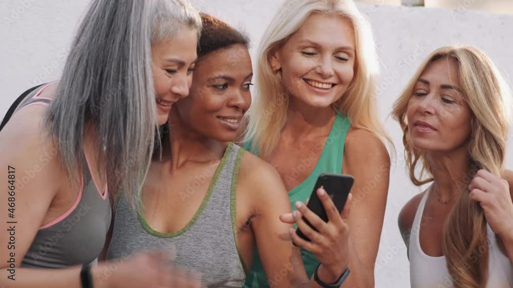Smiling multinational adult women looking at the phone outdoors Smiling multinational adult women looking at the phone outdoors