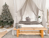 Christmas decorated rustic wooden bedroom interior in gray, white, silver colours with big baldaquin bed, fake fur blanket, candles, Christmas fir tree and gifts on floor. Christmas morning
