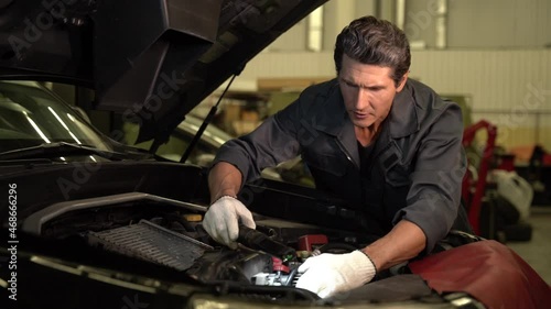 Waist up portrait view of the auto mechanic man with lamp working at the workshop while looking and repairing engine. Car service, repair and people concept