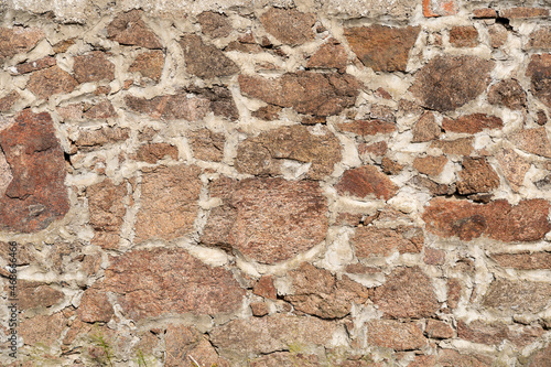 Vintage stone wall background texture. Old natural blocks of granite with different shapes filled with mortar to build a solid masonry. Exterior of an old building. Rough full frame backdrop.