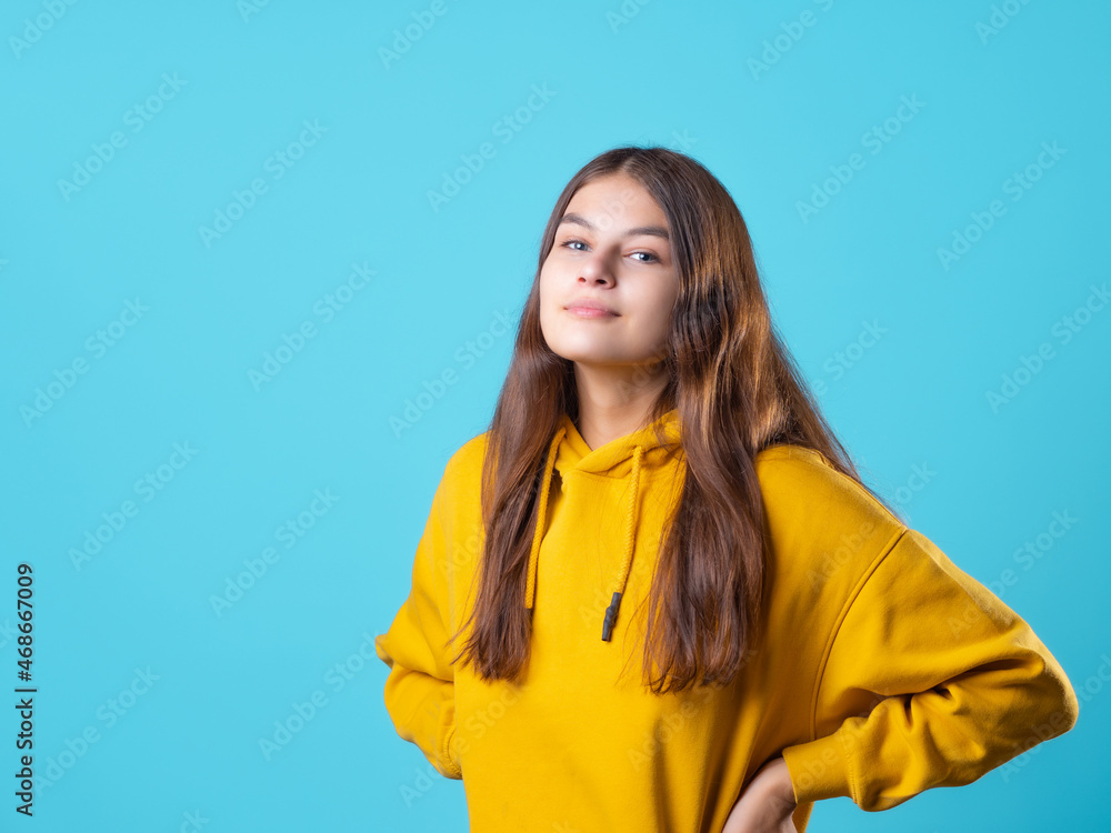 A beautiful young brunette in a yellow oversize hoodie, a positive student in a bright outfit, portrait on a blue background A beautiful young brunette in a yellow oversize hoodie, a positive student in a bright outfit, portrait on a blue background
