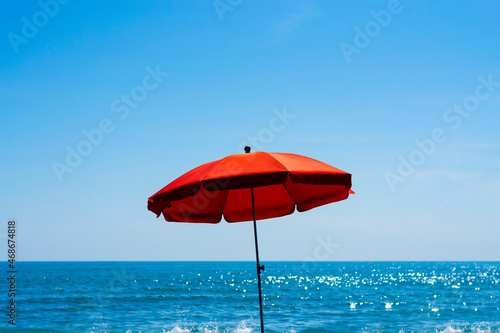 A lonely bright red beach umbrella in the center of the picture on a sunny summer day with blue sea and the sky in the background. Summer concept.