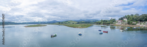 Paisaje panorámico de San Vicente de la Barquera con barcas en el agua,  y el reflejo de las nubes y montañas al fondo, en Cantabria, España, en el verano de 2020.