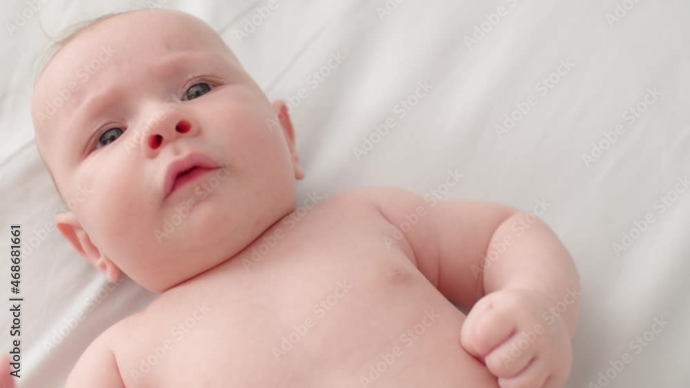 Beautiful newborn baby. Cute two-month-old baby with bare belly looks into camera, slow motion. Active newborn boy lies on the bed and moves his arms. High angle view of a chubby male baby.. Beautiful newborn baby. Cute two-month-old baby with bare belly looks into camera, slow motion. Active newborn boy lies on the bed and moves his arms. High angle view of a chubby male baby..