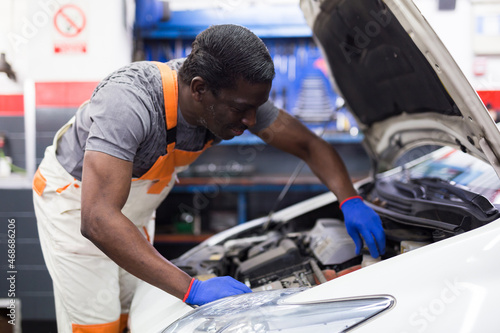 Professional american mechanic man in uniform repairing car engine in auto repair shop garage