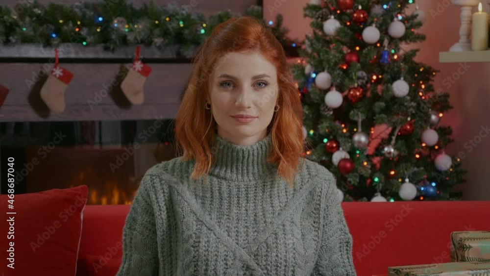 Smiling young beautiful woman portrait holding Christmas gift box on background of xmas lights decorated room and Christmas tree. Female looking at camera, red hair, blue eyes. Smiling young beautiful woman portrait holding Christmas gift box on background of xmas lights decorated room and Christmas tree. Female looking at camera, red hair, blue eyes.