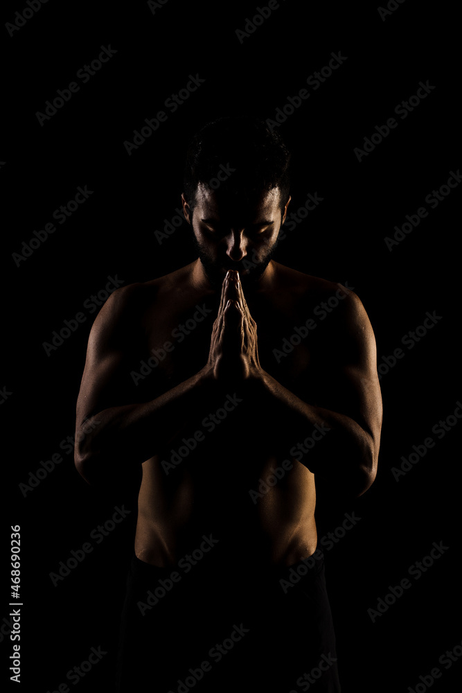 Naklejka premium Side lit muscular Caucasian man silhouette. Athlete praying against black background.
