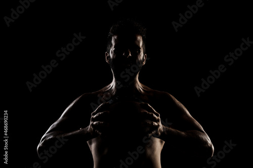 Basketball player holding a ball against black background. Side lit muscular Caucasian man silhouette