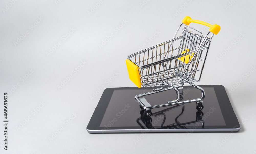Miniature shopping cart on a tablet on a gray background with copy space