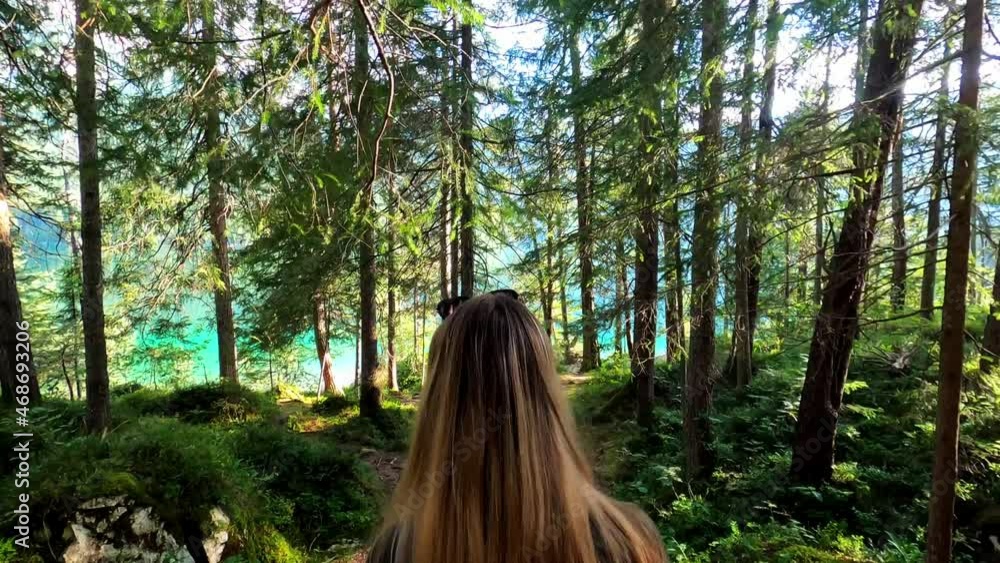 Third person view of a caucasian girl with blonde hair and a green dress, walking through a forest towards the famous lake Eibsee in Germany. Third person view of a caucasian girl with blonde hair and a green dress, walking through a forest towards the famous lake Eibsee in Germany.