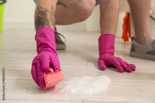 Young man with sponge cleaning floor in bathroom, closeup