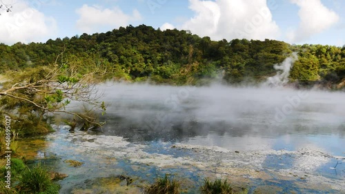 Panning shot of Toxic Steam flying over Frying Pan Lake with green mountains in background - Waimangu Volcanic Rift Valley in New Zealand - 4K