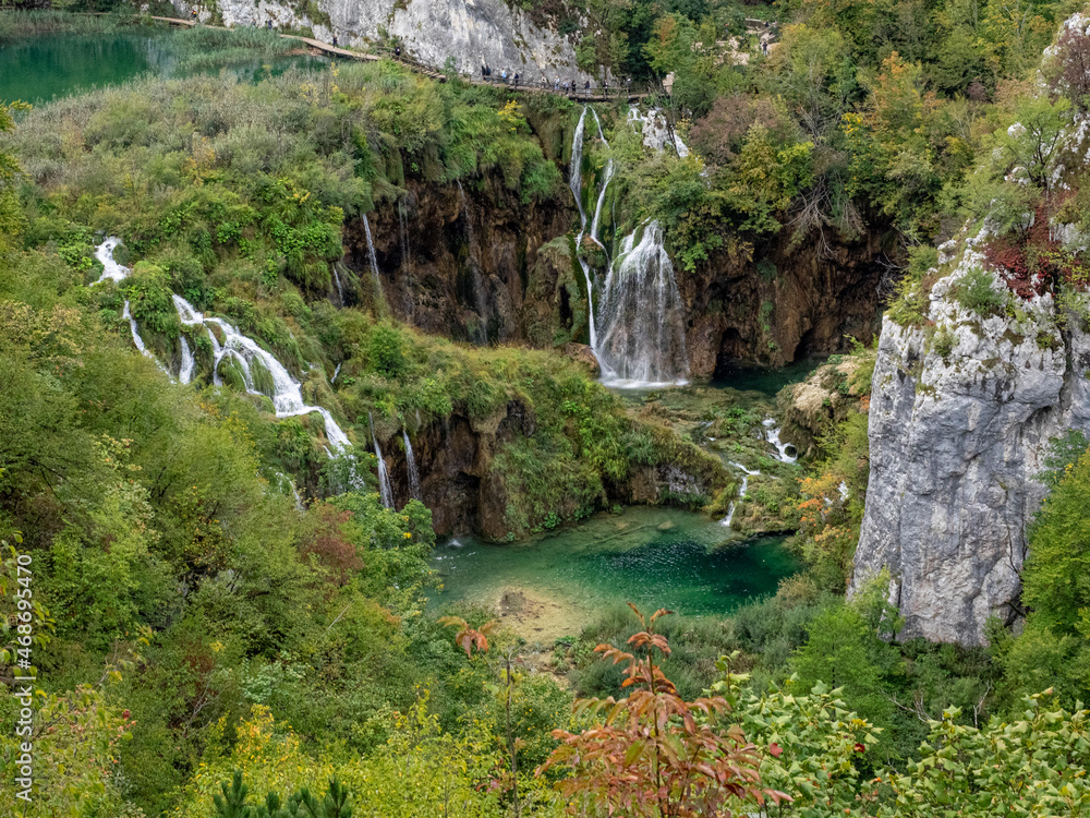 Water falls into lake surrounded. by rocks and trees in the Plitvice Lakes District, Croatia.