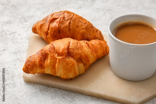 Board with delicious croissants and cup of coffee on light background