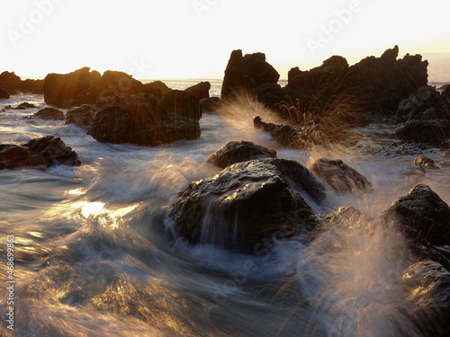 Motion effect, waves crashing rocks on the beach at sunset.