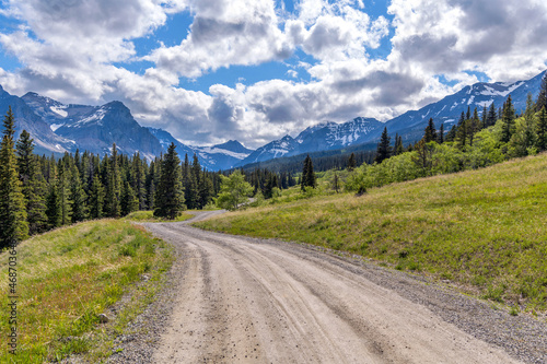 Spring Mountain Road - A dirt country road winding in Cut Bank Valley towards high peaks of Lewis Range on a sunny Spring Evening in Glacier National Park, Montana, USA.