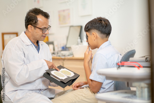 Ophthalmologist or optical staff use book of color blindness test with Indian boy to test for continue the process in optical shop.