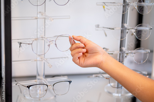 Close up hand of young people select glasses on shelf in optical shop. © narong