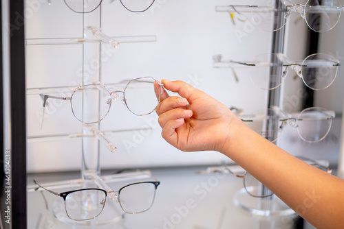 Close up hand of young people select glasses on shelf in optical shop.