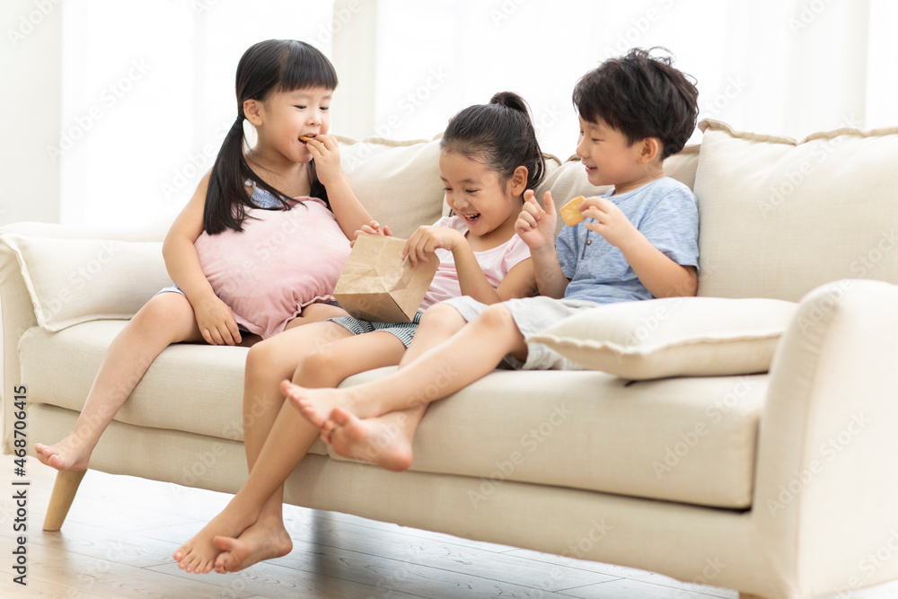 Cute Chinese children eating biscuits on sofa Cute Chinese children eating biscuits on sofa