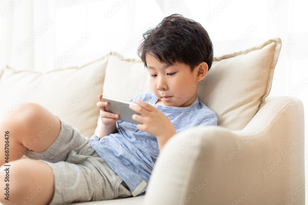 Cute little Chinese boy using smart phone on sofa Cute little Chinese boy using smart phone on sofa
